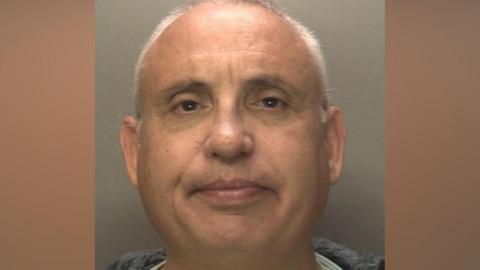 John Evans - a custody image of a clean-shaven man with short grey hair against a grey background.