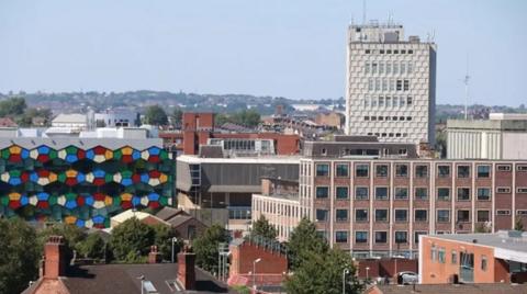 A view of Stoke on Trent from a tall building, with various multi-storey office blocks and one building decorated with multi-coloured patterns