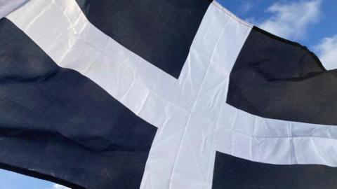 A photo of the Cornish flag. It has a white cross in the middle on a black background. 