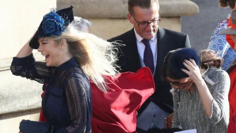 Wedding guests hold on to their head wear