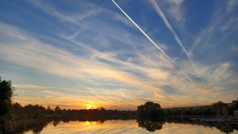 The sun rising over water with blue sky and white streaks of cloud 