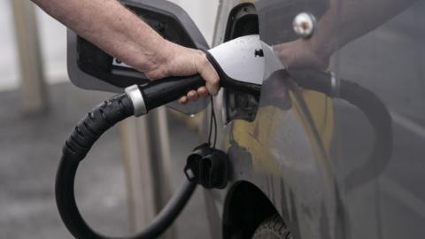 A man's arm holding a cable charging his electric vehicle at a charging station