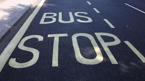 A sign saying Bus Stop in yellow painted on an asphalt road