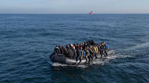 A black inflatable boat in a large body of water with a crowded group on it. 