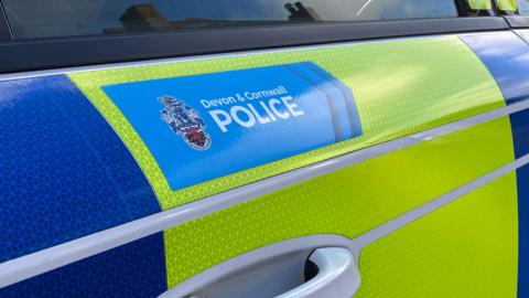 A blue and yellow fluorescent Devon and Cornwall Police car with the force's name on the side.