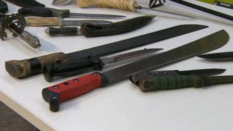 Various knives are laid out flat on a table in a room