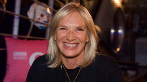 A happy woman smiling at the camera. She is wearing a black top.