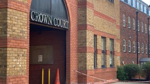 A modern red-bricked building with an arched entrance, with the words Crown Court overhead, and a four storey building attached.