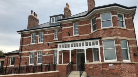 A large red-bricked two storey building. There are steps and a porch at the front.