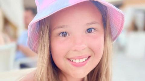 Imogen, who is 12, wears a pink sun hat and is smiling at the camera
