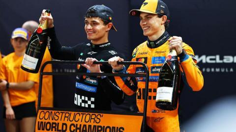Lando Norris and Oscar Piastri celebrating after McLaren won the constructors' championship, holding up a board saying 'Constructors' world champions 2025' 
