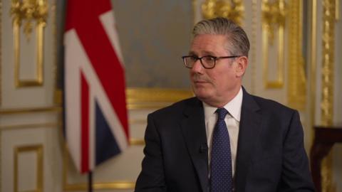 SIr Keir Starmer sits in an ornate room with a Union Jack in the background