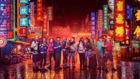 Five pairs of travellers stand in a line surrounded by neon lights.