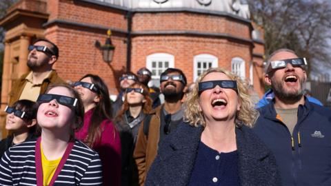 A group of people at the Greenwich Observatory in London observe a solar eclipse using spevcial glasses