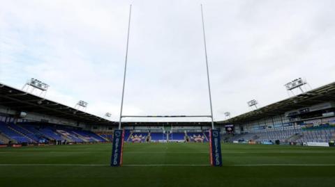 The inside of the Halliwell Jones Stadium, with pitch and goalposts and tiered seating in view.