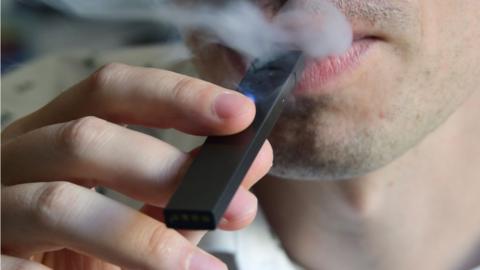 An illustration shows a man exhaling smoke from an electronic cigarette