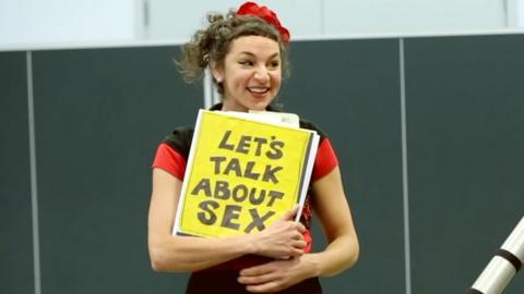 Woman holding a sign saying 'Let's talk about sex'