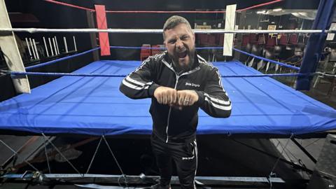 Wrestler Zek Bevis standing in front of a wrestling ring