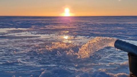 Seawater pump floods the surface of the sea ice with seawater as the Sun sets