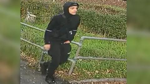 Man in black tracksuit with hood up on CCTV