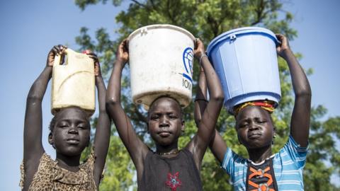 Girls, each carrying a container of water on her head, stand outdoors in the city of Bentiu, capital of Unity State on June 2, 2016.