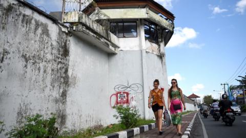 Two foreign tourists walk alongside the perimeter wall of the Kerobokan prison