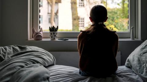 Anonymous girl looking out of a window, viewed from behind