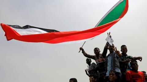 A group of protesters fly the Sudan flag
