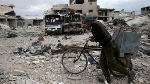 A Syrian man pushes his bike past destroyed buildings in the besieged rebel-held town of Douma on 30 March 2018