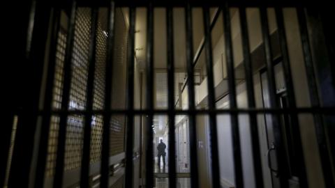 A guard stands behind bars at a prison