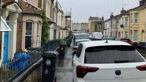 A photo of cars parked on the pavement, narrowing the street.
