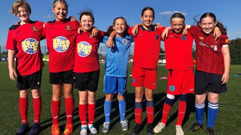 From left to right, Jemima, Maisy, Dulcie, Olive, Poppy, Lois and Cate, standing together in their football kits