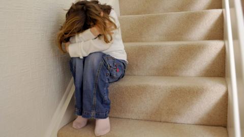 A child with her head in her arms on the stairs.