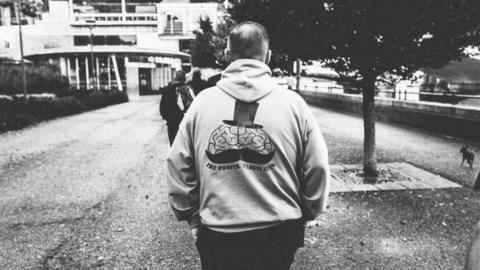 A man wearing a hoodie with the The Proper Blokes Club logo walks with his back to the camera