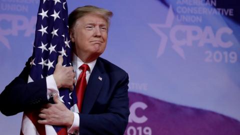 Donald Trump hugging a US flag at the Conservative Political Action Conference in Maryland, March 2019