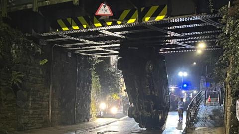 Van stuck vertically under railway bridge