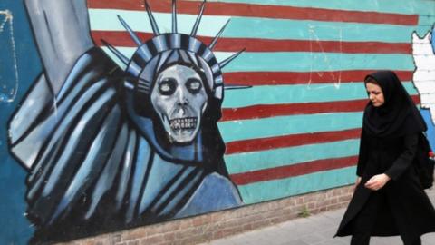 An Iranian woman walks past a mural on the wall of the former US embassy in the Iranian capital