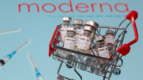 A small shopping basket filled with vials labelled "COVID-19 - Coronavirus Vaccine" and medical syringes are placed on a Moderna logo in this illustration taken November 29, 2020