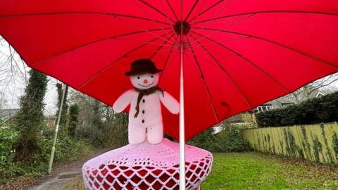 A snowman post box topper with a red umbrella