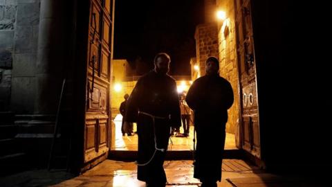 Franciscan friars walking through large wooden doors of Church of the Holy Sepulchre