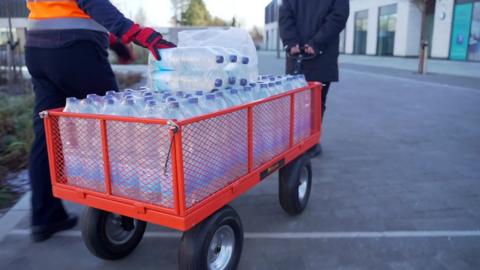 Two people pulling a cart loaded with bottles of water