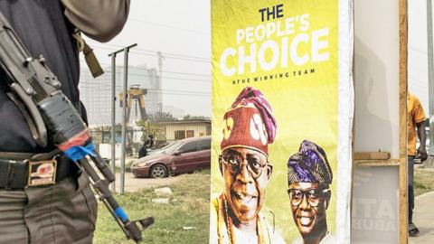 A security guard stands next to an election poster for Bola Tinubu in Lagos, Nigeria - February 2023