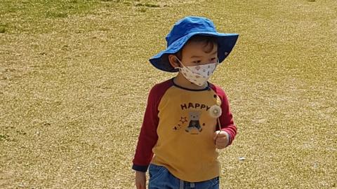 Small boy wearing floppy blue hat and face mask walking on grass