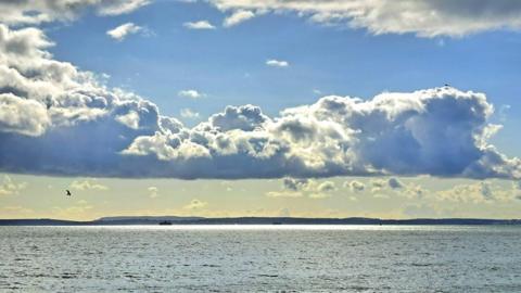 A flat-bottomed layer of grey and white cloud stretches across the sky which is blue above and a golden colour below. It’s all reflected off the sea which stretches out underneath.