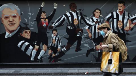 Man with mask walks past Newcastle United mural