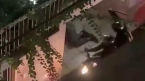 Screengrab from a video showing an Iranian riot police officer raising a baton before beating a man lying on a street in Tehran, Iran