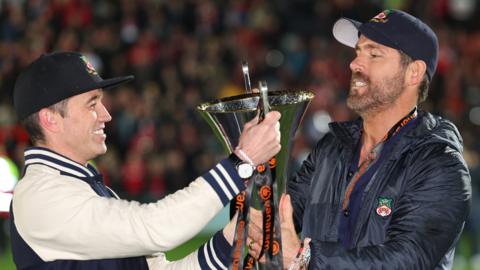 Rob McElhenney and Ryan Reynolds hold Wrexham's National League trophy