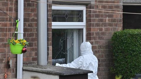 A forensic officer examines a broken window