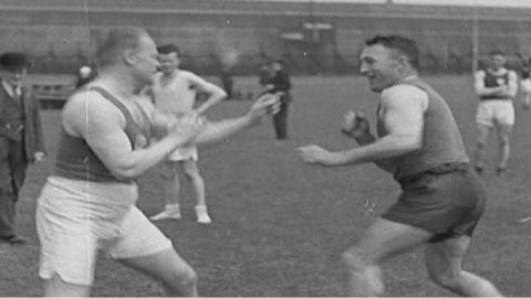 Black and white archive footage of two men fist fighting