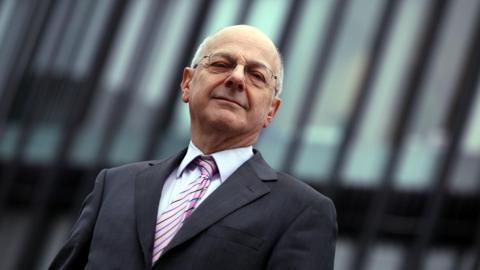 Close-up of Lord Beecham looking into the camera. He is wearing glasses, and a dark suit with a light shirt and pink tie.